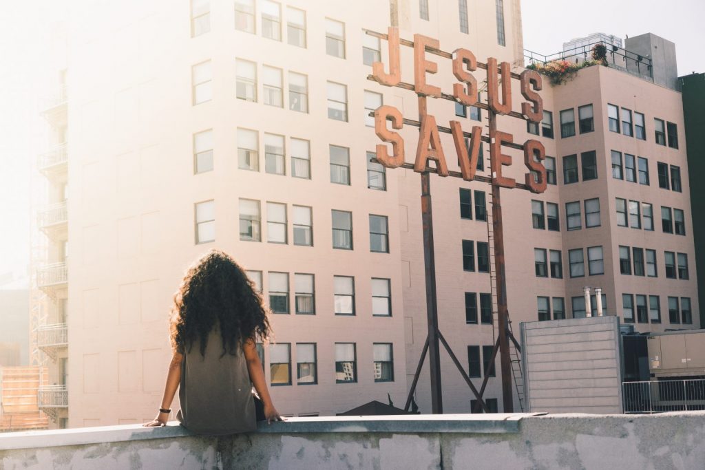 Woman sitting on a rooftop looking at "Jesus Saves" sign